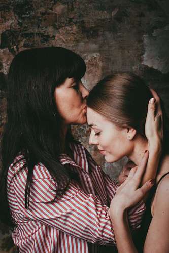 kissing-forehead a mother kissing her daughter with a broken wall in the background