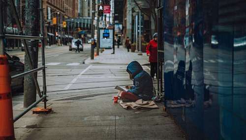 homelessness destitute person sitting on the street reading a newspaper