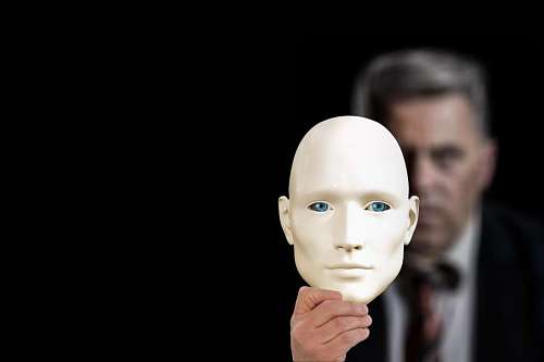 close-up of a mask held by man from behind with black studio background