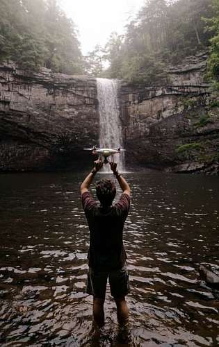 inhaling man holding a drone in front of a waterfall