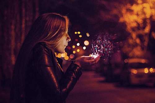 mujer soplando brillos de sus manos en la calle de noche