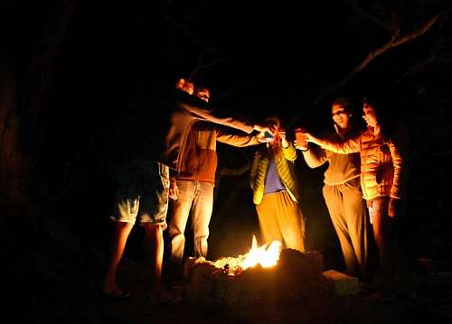 Group of people toasting on a fire pit on the beach at night