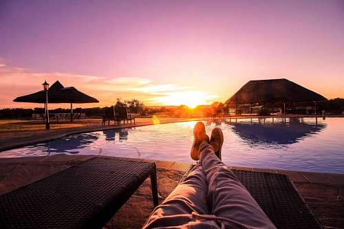 Man sitting on a deck chair in front of a swimming pool at sunset