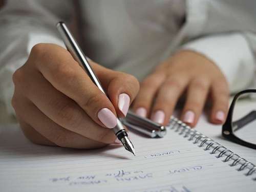 handwriting Woman in White Long Sleeved Shirt Holding a Pen Writing on a Paper