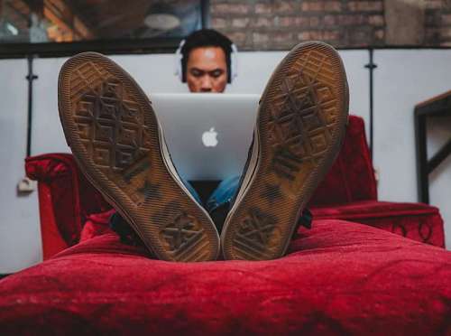 close-up of a man's shoes lying on his bed using his laptop