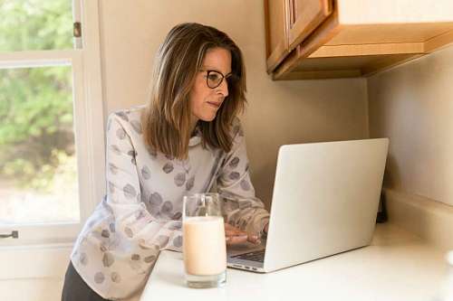 adult woman uses her laptop in the cupboard while having a glass of milk