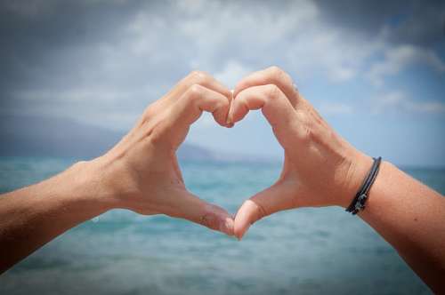 Man's hands forming a heart on the beach